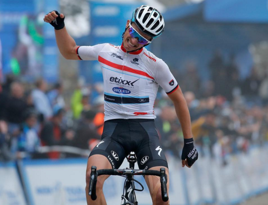 Cyclist celebrates victory by raising a fist while riding a bicycle. Wears a helmet and an Etixx Quick-Step jersey.
