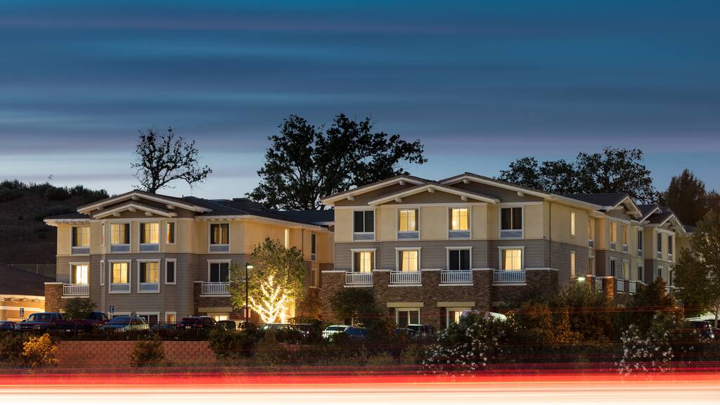 Hotel building illuminated at night with warmly lit windows. It stands against a twilight sky, surrounded by trees and bushes.