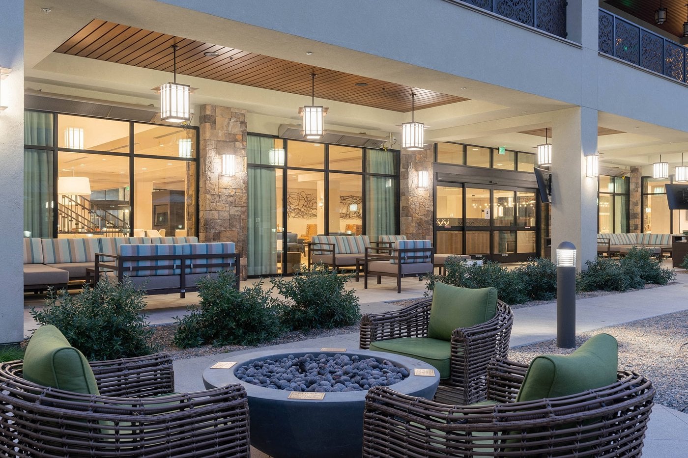 Outdoor patio with wicker chairs around a round fire pit, set in a modern hotel environment.