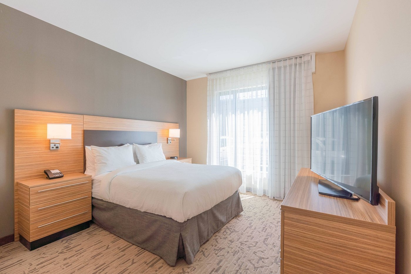 Modern hotel bedroom featuring a neatly made bed with white linens, flanked by wooden nightstands and lamps.