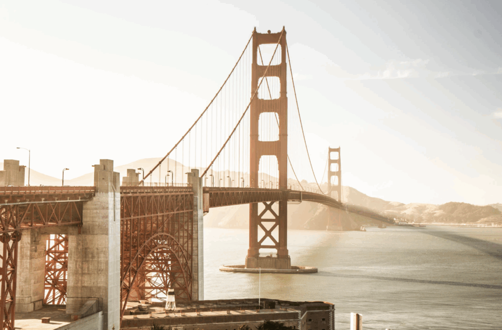 Golden Gate Bridge towers majestically over glistening water, with sunlight highlighting its iconic orange-red structure.