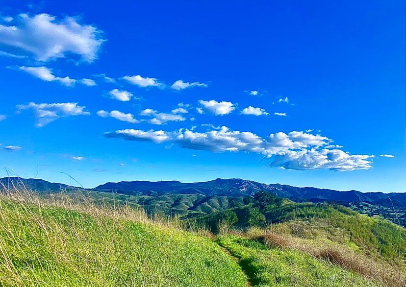 Green hills stretch beneath a vivid blue sky, scattered with fluffy white clouds.