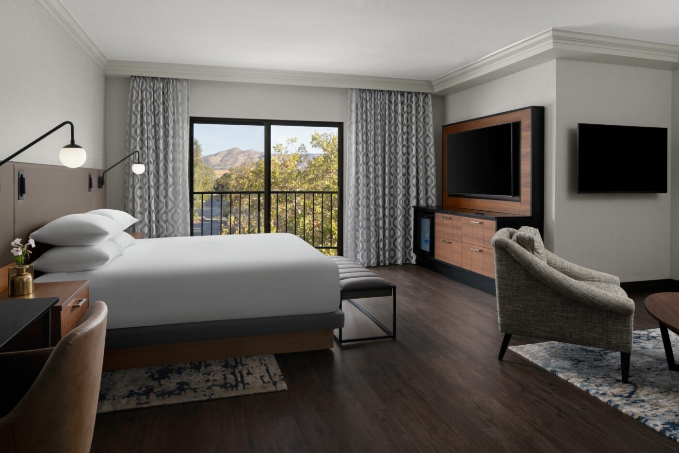 Modern hotel room with a large bed, wall-mounted lamps, and a TV area.