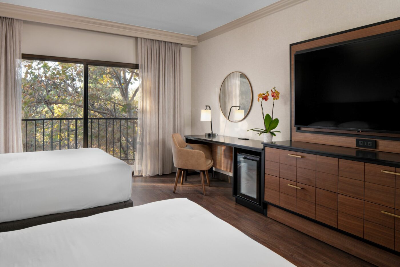 Hotel room with two beds and a desk featuring a lamp and orchids.