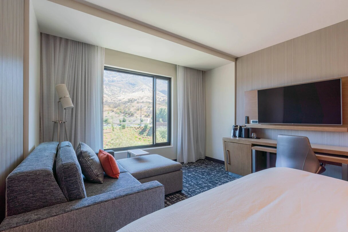 Modern hotel room with a gray sofa beside a window showcasing a mountain view.