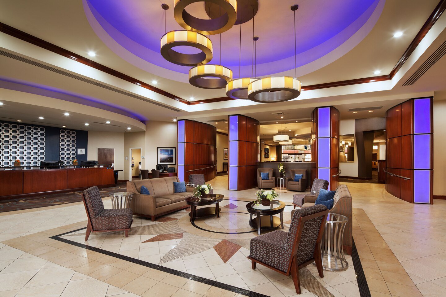 Luxurious hotel lobby featuring plush seating around coffee tables, illuminated by overhead circular chandeliers.