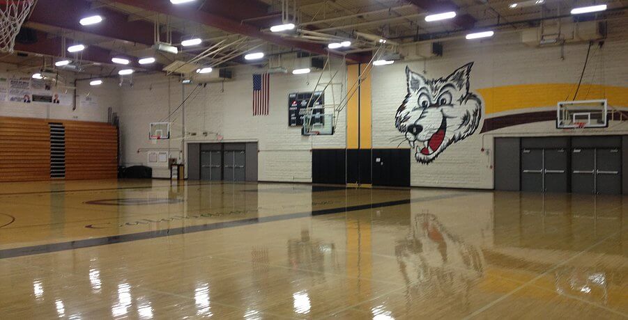 Basketball court featuring a polished wooden floor, surrounded by bleachers and multiple hoops.