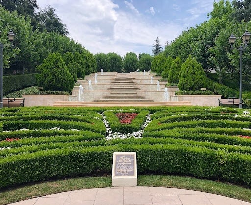 Terraced garden features cascading fountains on stone steps, surrounded by manicured hedges and vibrant flowerbeds.
