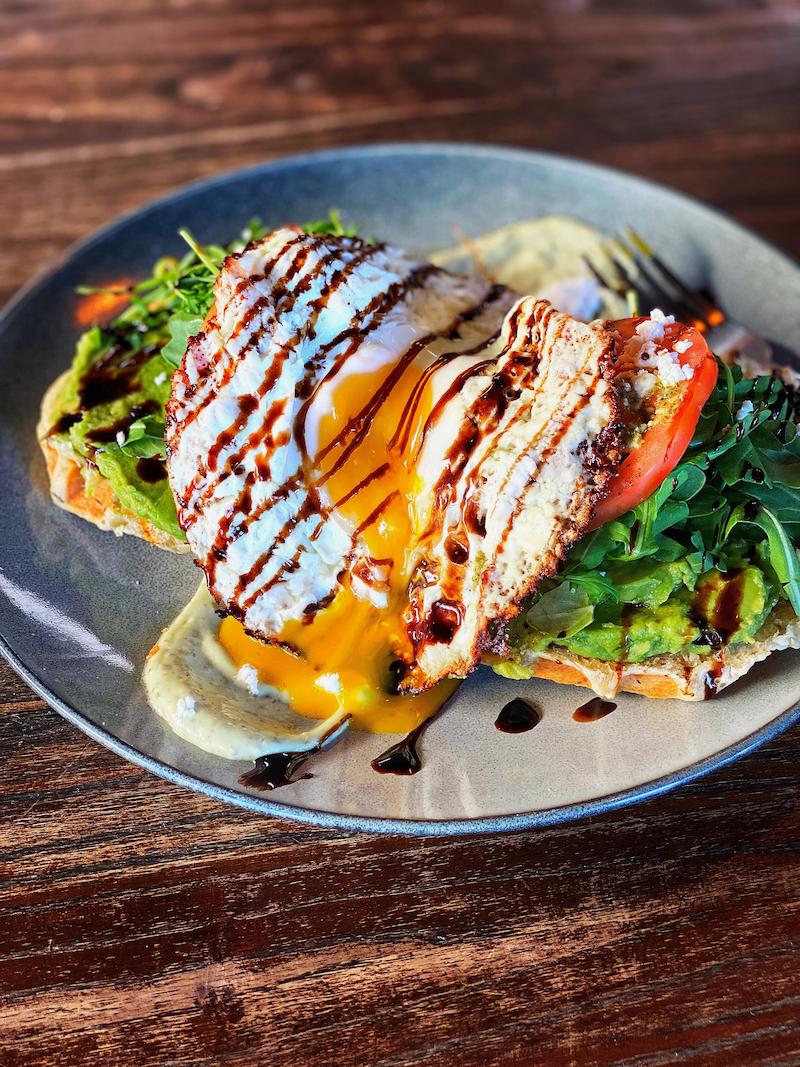 Open-faced sandwich features a poached egg drizzled with balsamic glaze, yolk oozing over avocado toast.