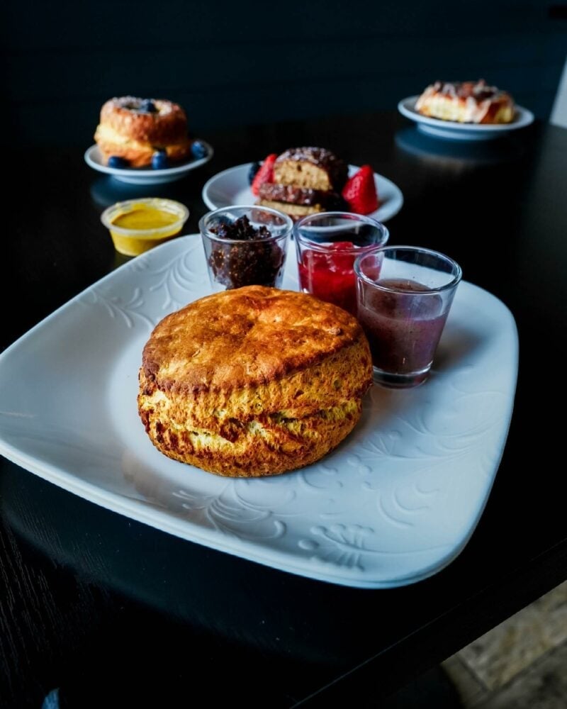 Scone sits on a decorative white plate, accompanied by three small cups of jam.