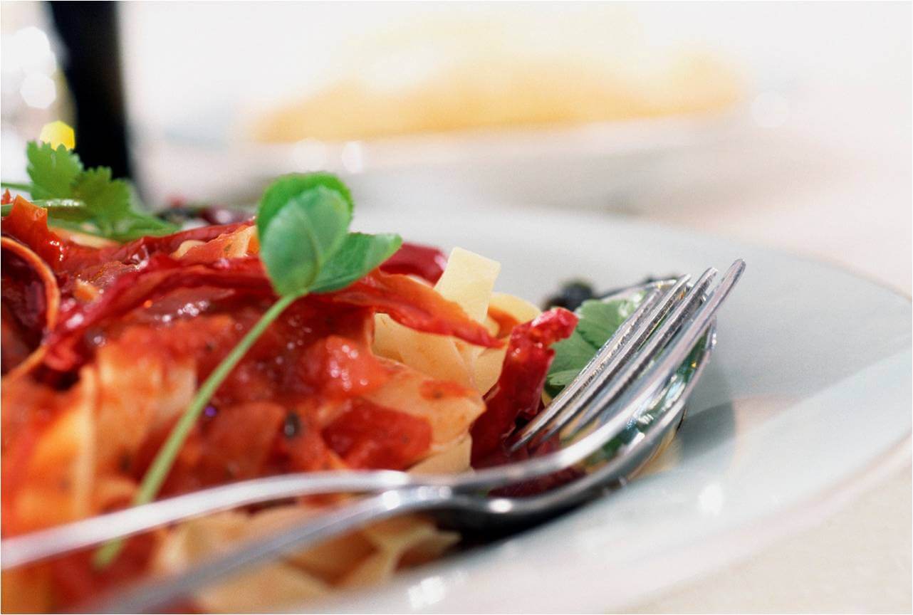 A fork rests on pasta topped with red tomato sauce and garnished with fresh herbs on a white plate with a vibrant dining presentation in Conejo Valley.
