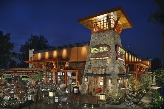 Lazy Dog Restaurant & Bar is illuminated at night, featuring rustic architecture with stone and wood elements.