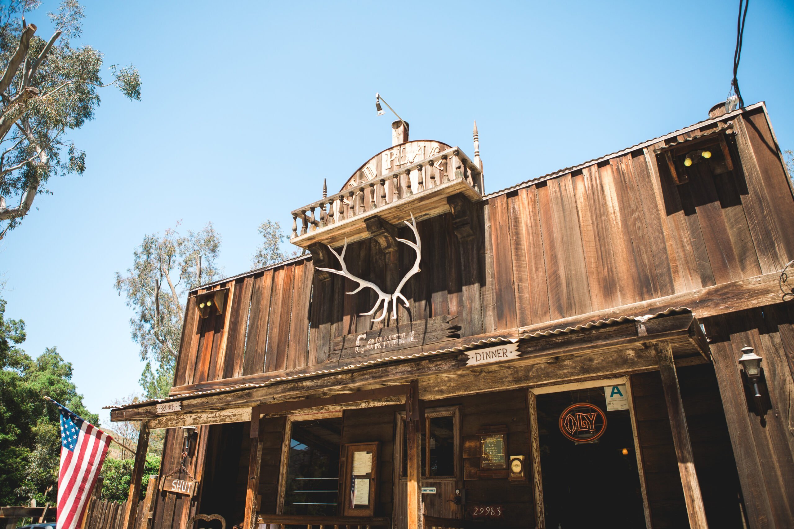 Rustic wooden building displays large antler sculpture above the entrance. "29983" and "DINNER" signs are visible.