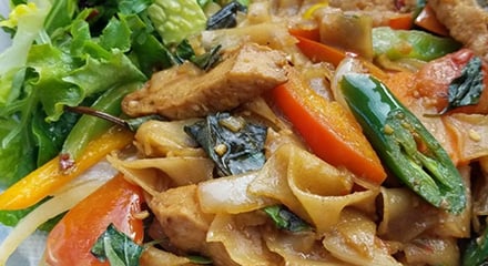 Stir-fried noodles with tofu, bell peppers, and basil are garnished with fresh salad greens with a vibrant and colorful dish.