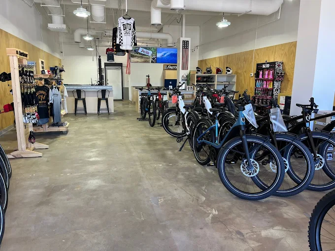 Bicycles displayed in a well-lit showroom with wooden and white walls, surrounded by cycling apparel and accessories.