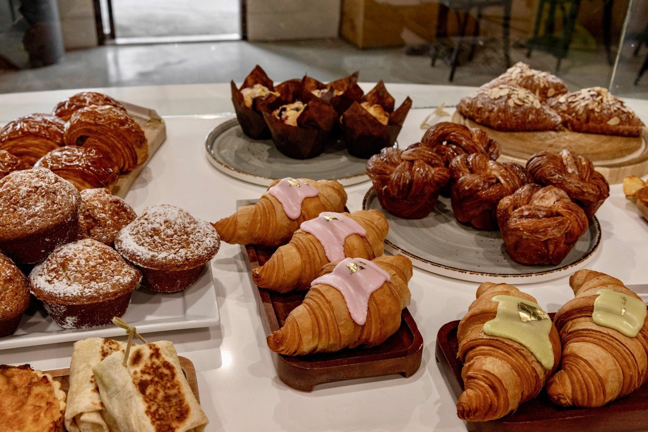 Assorted pastries and croissants displayed on plates and trays at a café counter.