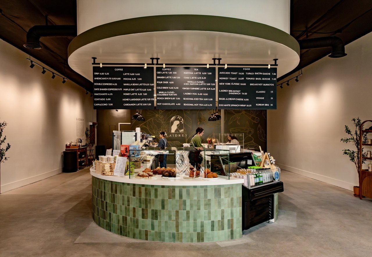 Interior of a modern café with a curved counter, pastry display, and menu boards overhead.