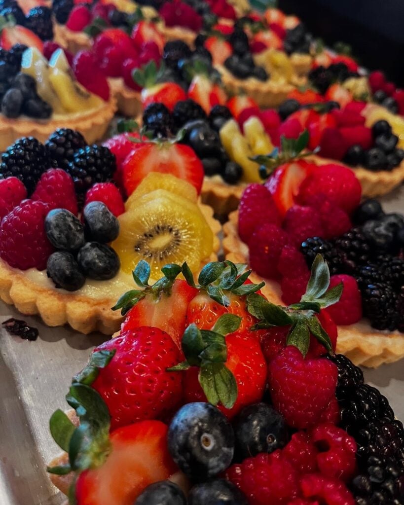 Assorted fresh fruit tart pastries with strawberries, blueberries, raspberries, and kiwi at Historia Bakery Cafe in Thousand Oaks