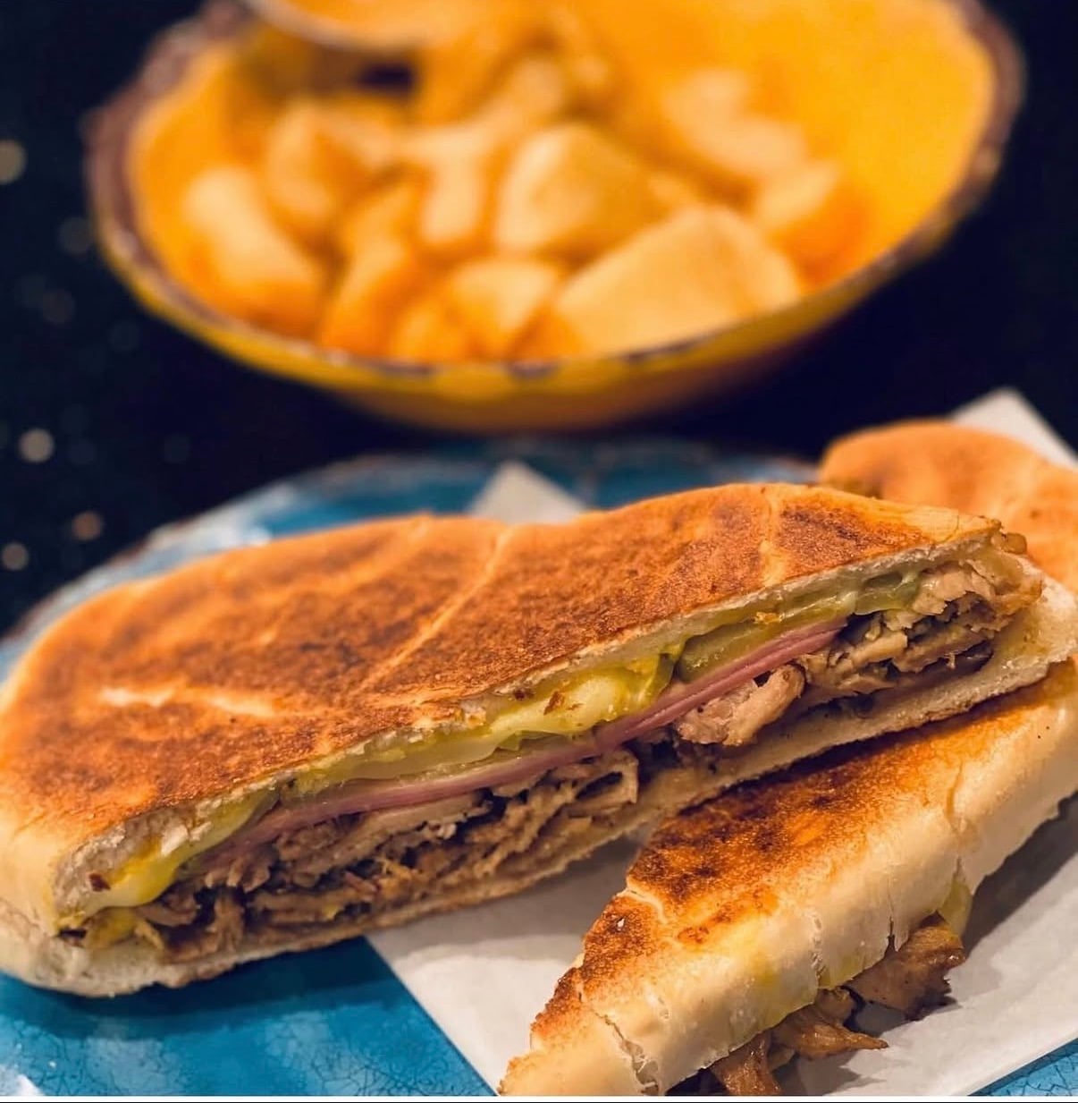 Pressed Cuban sandwich filled with roasted pork, ham, cheese, pickles, and mustard, served with plantain chips.