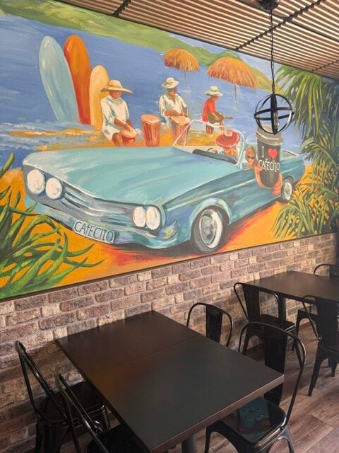 Colorful mural of a vintage convertible, musicians, surfboards, and a coffee cup celebrating Cuban café culture.