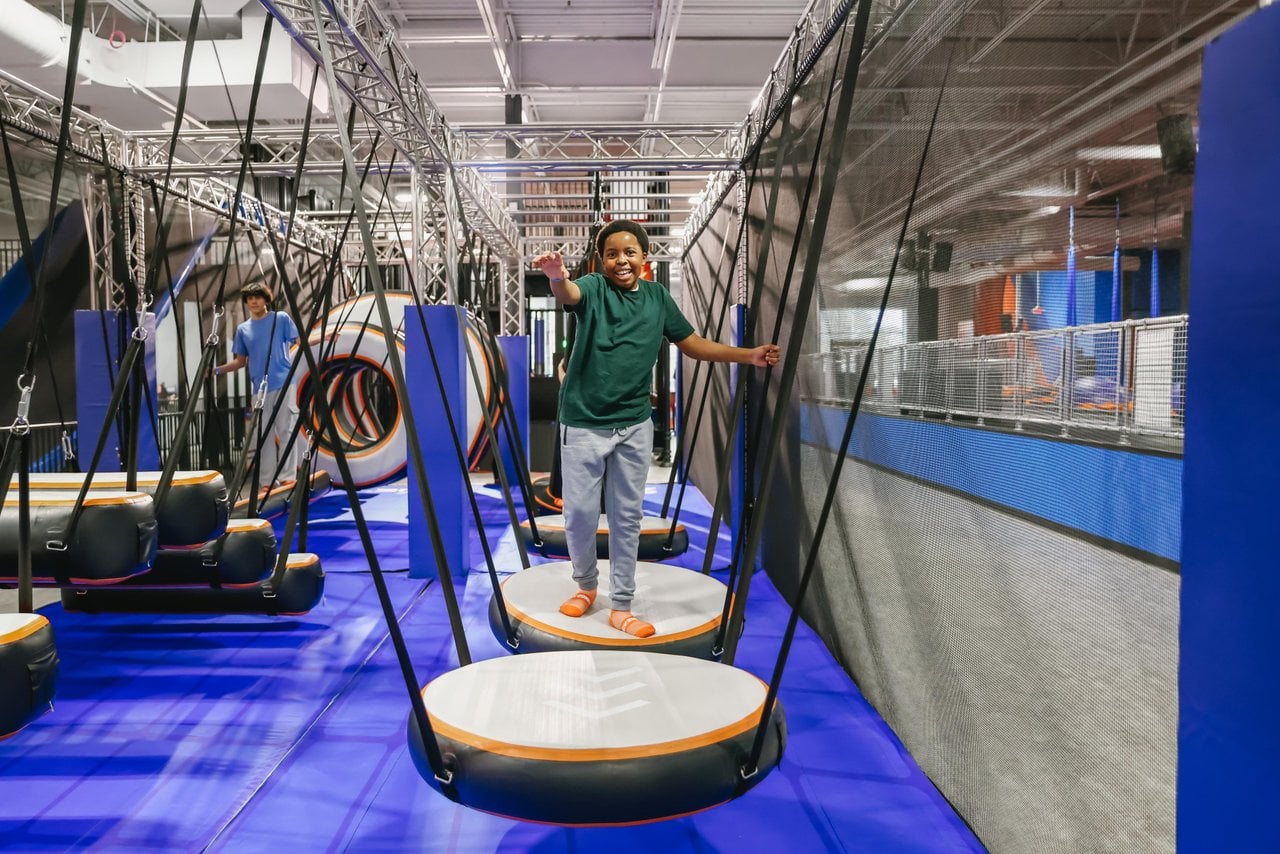 Alt text: Child balances across suspended platforms on the Sky Zone ninja obstacle course.